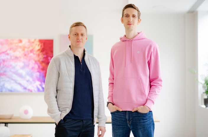 Two people standing side by side in front of a presentation screen, in a modern indoor workspace.